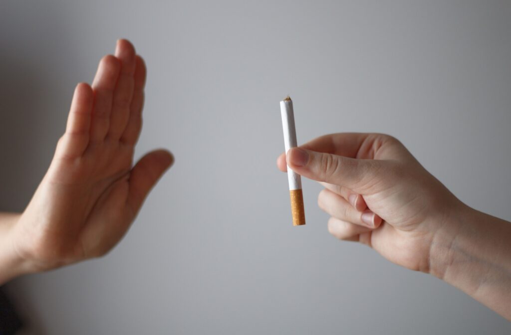 A close-up image of a hand saying no to an offered cigarette over a gray background.