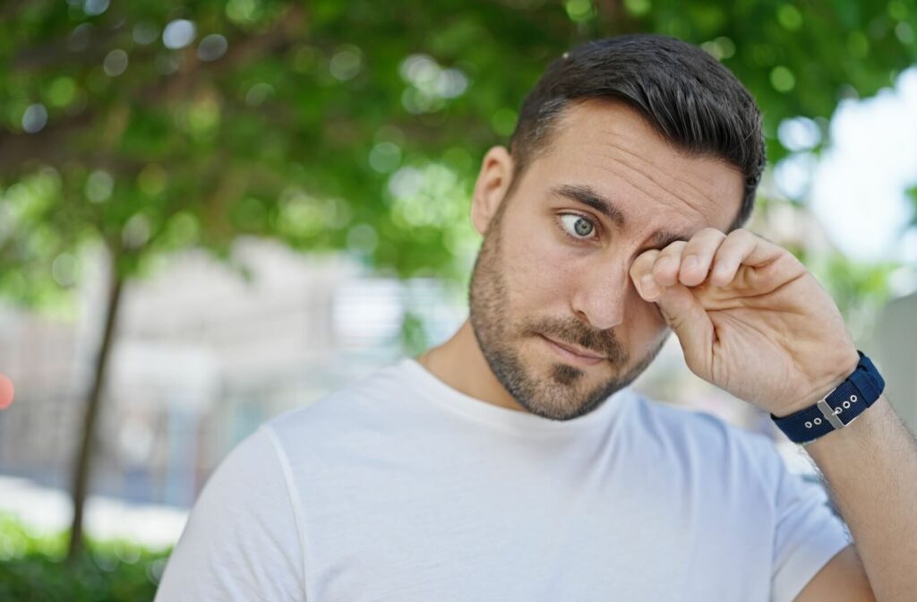 A person outdoors rubbing their eye, possibly experiencing discomfort or irritation.