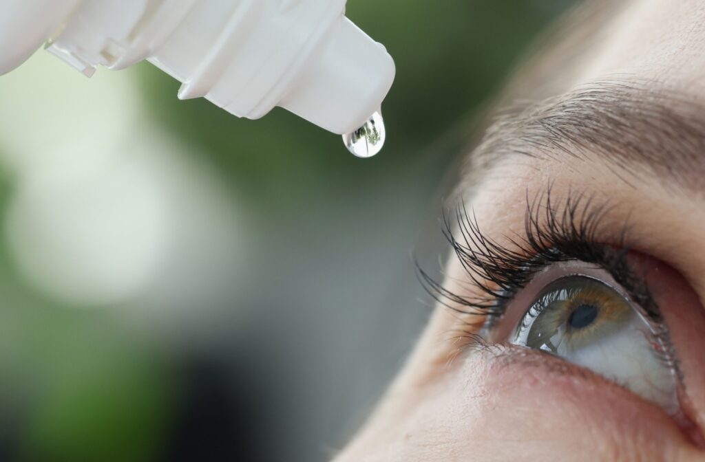 Closeup of someone putting eyedrops into their eyes, with a blurred outside background.