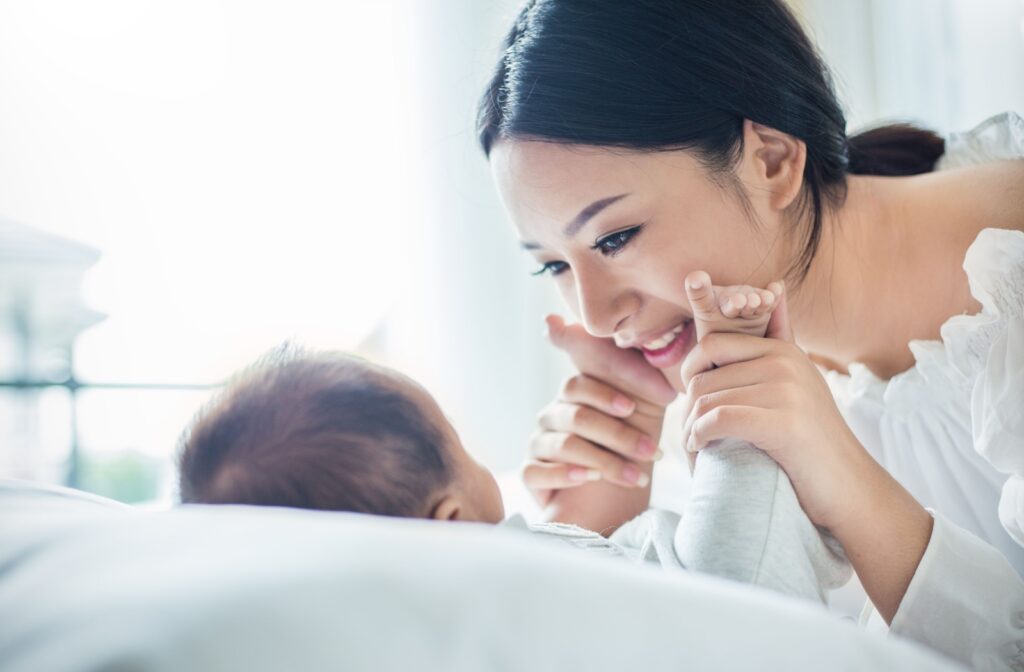 A mom looking down loving at their newborn baby as they hold the baby's feet up to their cheeks.