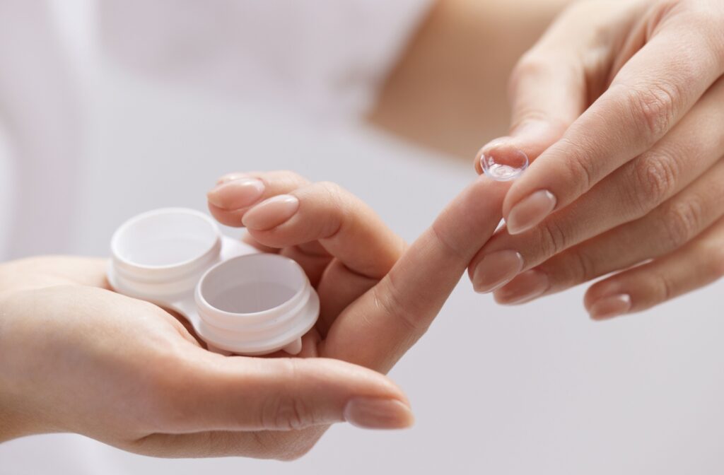 A person holds a contact lens on the tip of their finger above an open contact lens case.