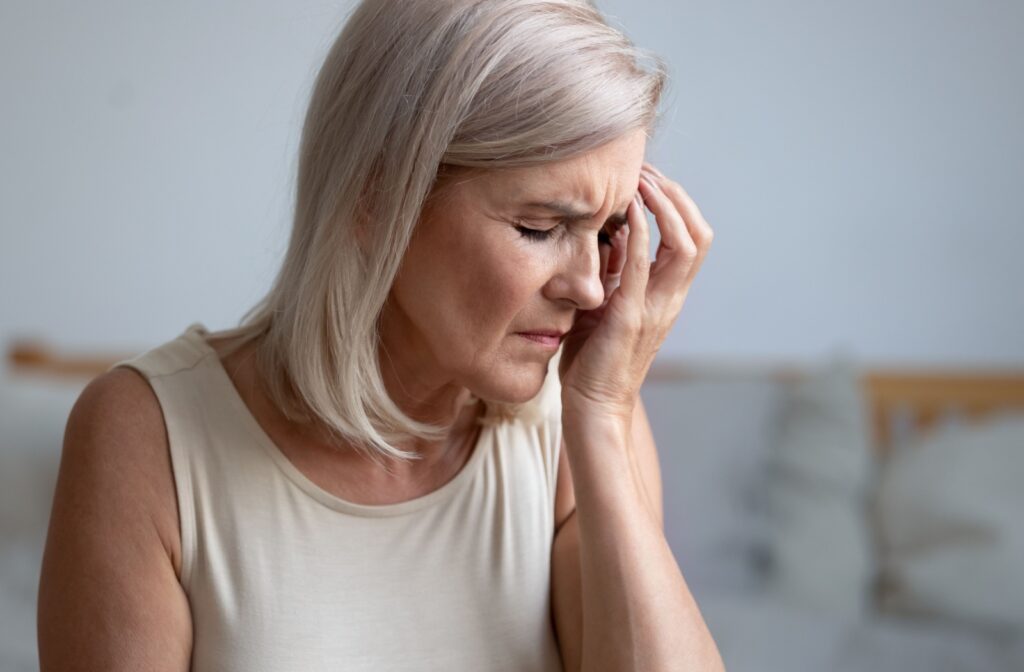 An older adult holds her left eye in discomfort, likely from unilateral dry eye.