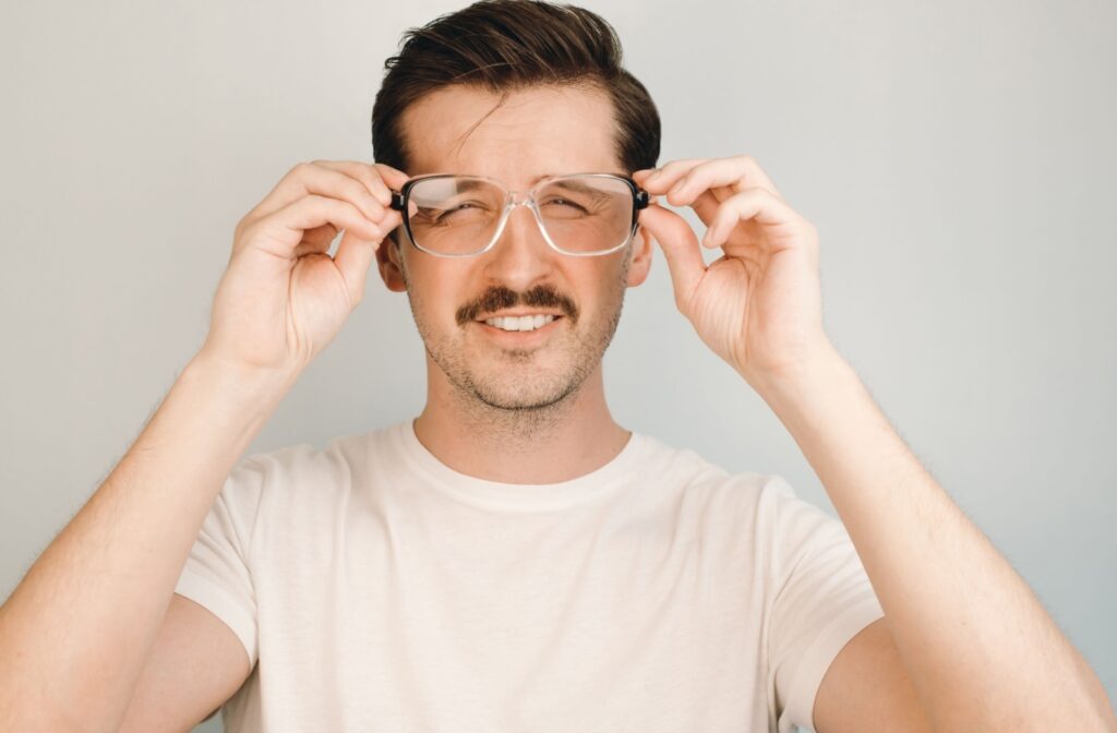 A man squinting to see while looking through a pair of eyeglasses.