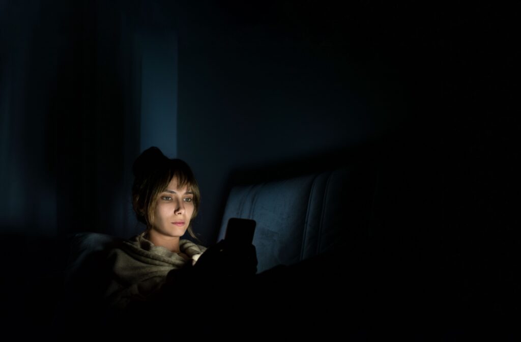 A person sitting in the dark, starring at their phone screen up close, which can contribute to the progression of myopia.