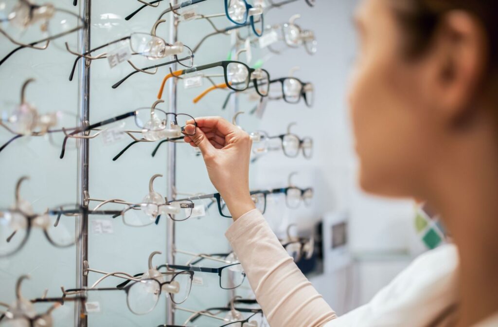 A person selecting a pair of glasses from a wall of frames at their local optometrist's office.
